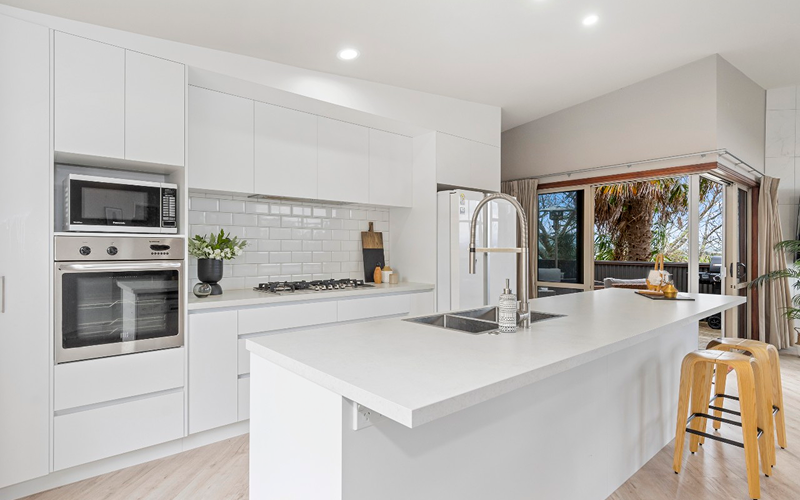 A modern kitchen featuring white cabinets and a stainless steel sink, showcasing a clean and bright design.