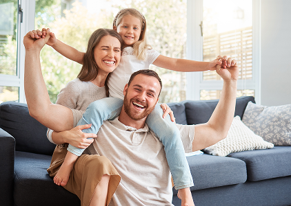 A man and woman sit on a couch with their two children, all smiling and enjoying family time together.