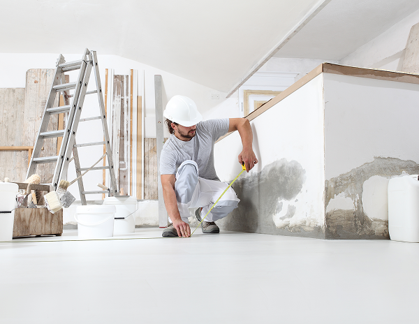 A man wearing a hard hat and helmet is actively working on a wall, focused on his task.